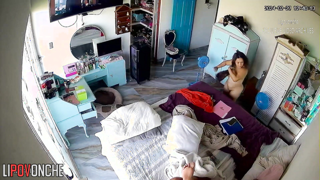A curvy brunette changes clothes in the bedroom in front of the TV