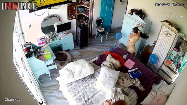 A curvy brunette changes clothes in the bedroom in front of the TV