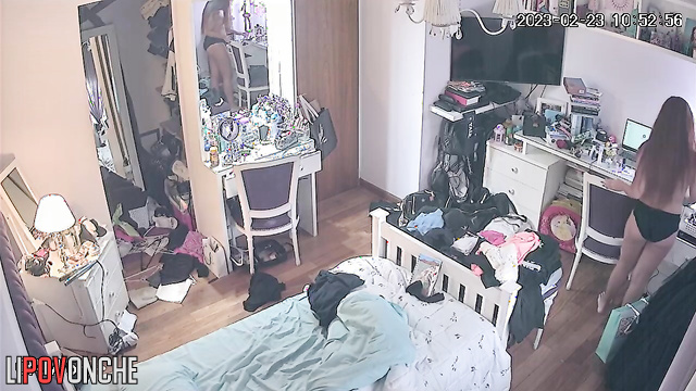 A long-haired redhead walks around her room with her breasts exposed