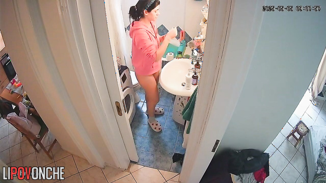 A curious girl looks at her bare bottom while standing on the toilet