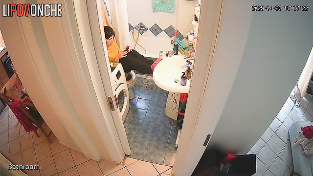 A young cutie has her legs up on the sink, sitting on the toilet with her bare ass