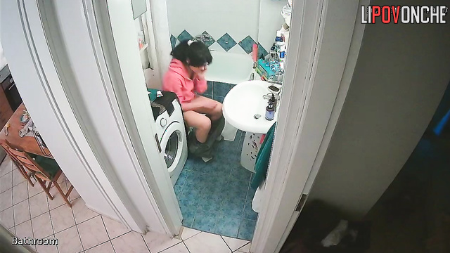 A girl, sitting on the toilet without panties, lifts her sexy legs high
