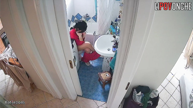 A beauty examines her shaved pussy while sitting on the toilet without panties