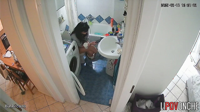 A cute brunette is drinking a Coke while sitting on the toilet