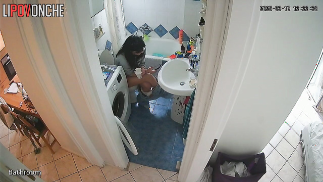 A cute brunette is drinking a Coke while sitting on the toilet