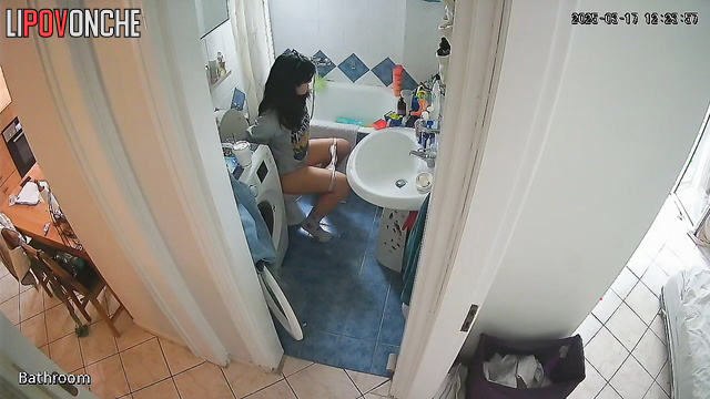 A cute brunette is drinking a Coke while sitting on the toilet