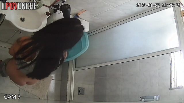 A long-haired, pregnant brunette is sitting on the toilet with her panties down
