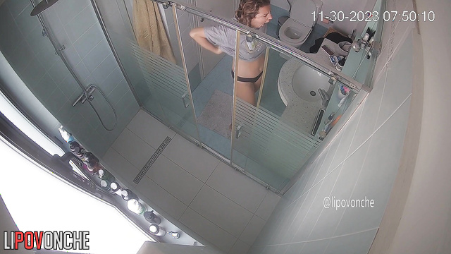 A bearded man is sitting on the toilet, watching his naked wife take a shower