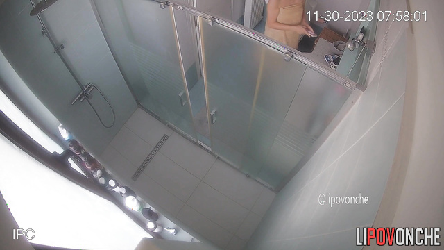 A bearded man is sitting on the toilet, watching his naked wife take a shower