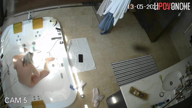 An older teacher with big tits washes her shaved pussy in the bathtub