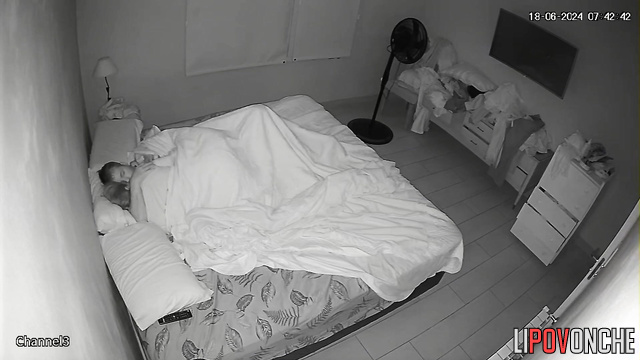 An unshaven man arouses his sleepy wife by playing with her nipples with his tongue