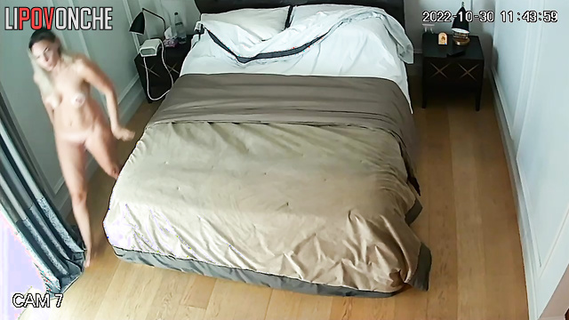 A naked, slender blonde with large breasts tidies up the bed after sleeping