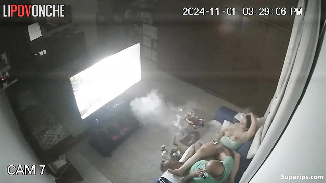 An elderly bald man plays with a voluptuous milf's wet pussy while watching TV