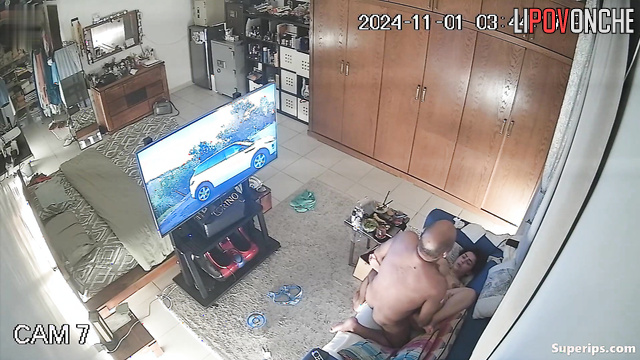 An elderly bald man plays with a voluptuous milf's wet pussy while watching TV